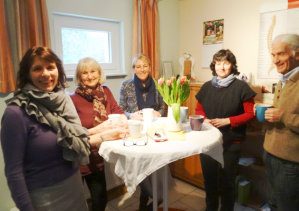 Feng Shui Ausbildungsgruppe Fünf lächelnde Personen stehen um einen Tisch mit Blumen und Getränken.