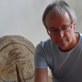 Seelenzaubern Mann mit Brille, der konzentriert für Menschen arbeitet, im Hintergrund eine runde Baumscheibe mit Riss.