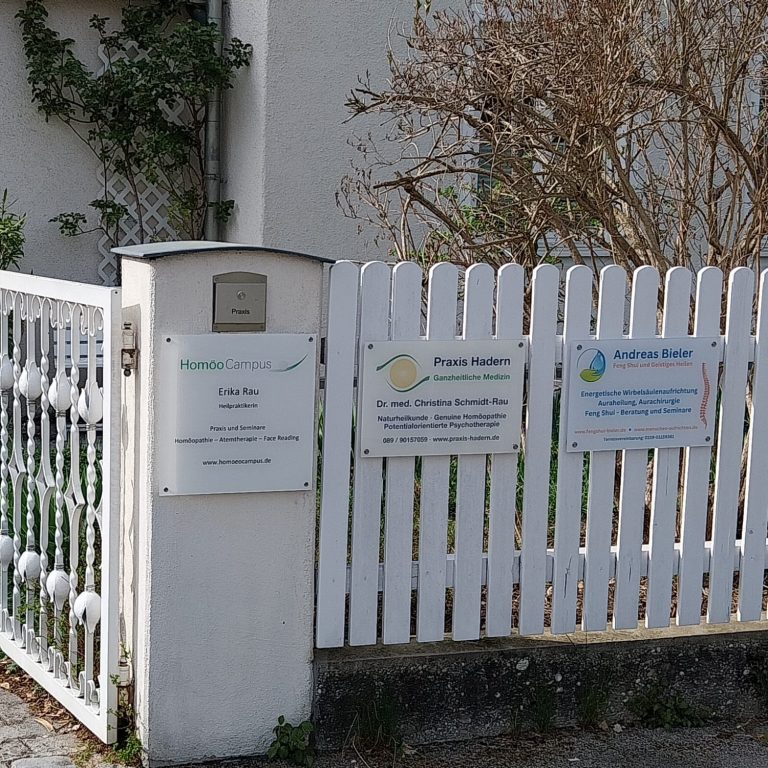 Weißer Zaun mit Schildern zur Erläuterung von Dienstleistungen und Kontaktinformationen.