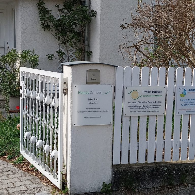 Weißer Lattenzaun mit Hinweisschildern vor einem Haus, umgeben von grünem Gras.