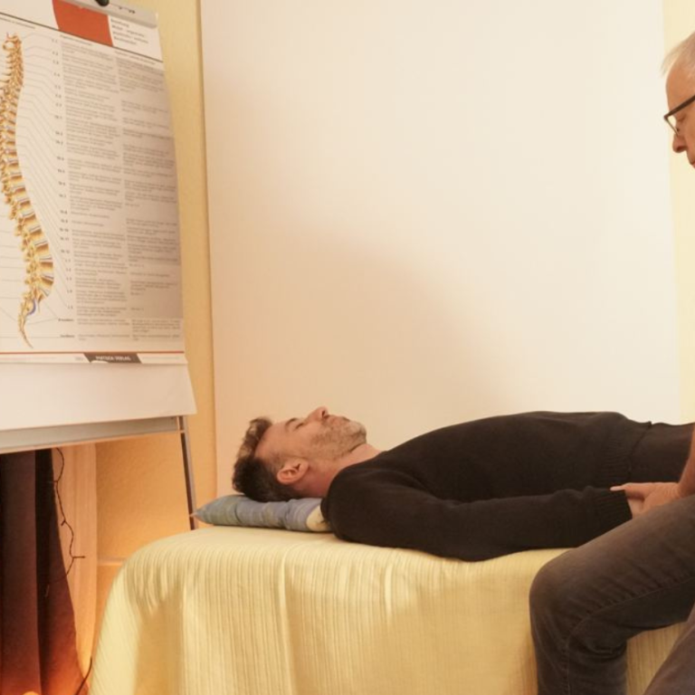 Zwei Personen in einem Raum, eine liegt auf einem Tisch, die andere sitzt daneben.