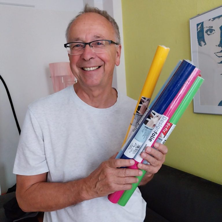 Ein lächelnder Mann hält bunte Farbrollen in seinen Händen.