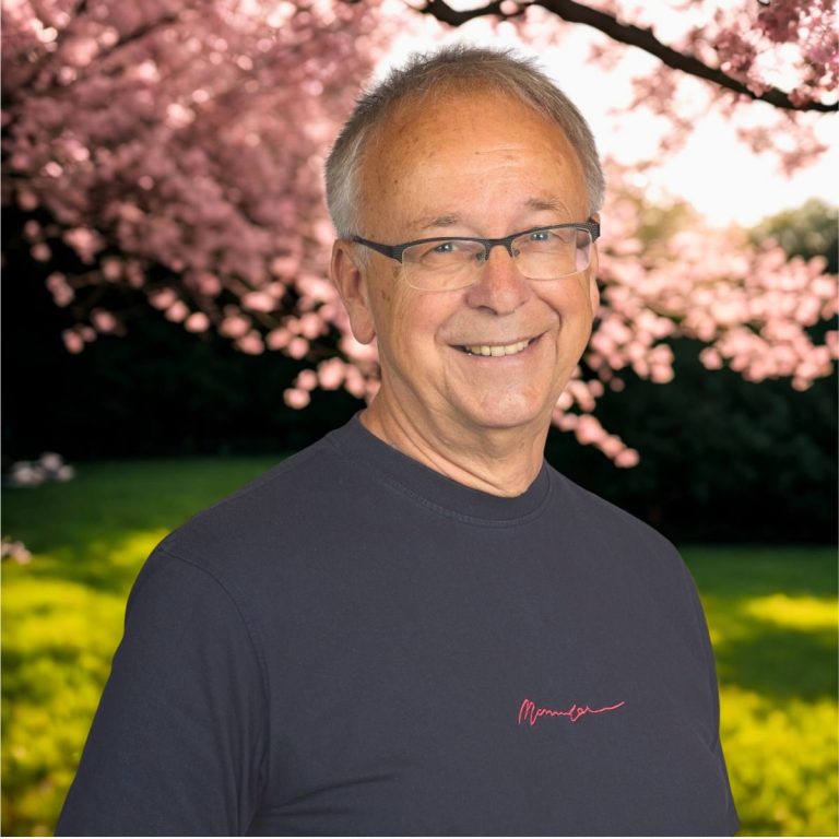 Andreas Bieler aus München Erfahrener Mann mit Brille, lächelnd vor blühenden Kirschbäumen im Hintergrund.