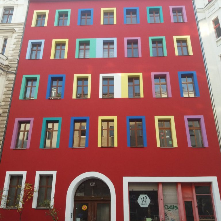 Rote Fassade mit bunten Fensterrahmen in verschiedenen Farben.