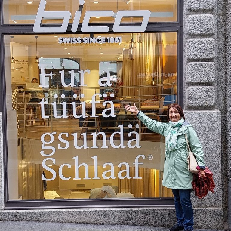 Frau in blauer Jacke steht vor einem Geschäft mit Schriftzug über gesunden Schlaf.