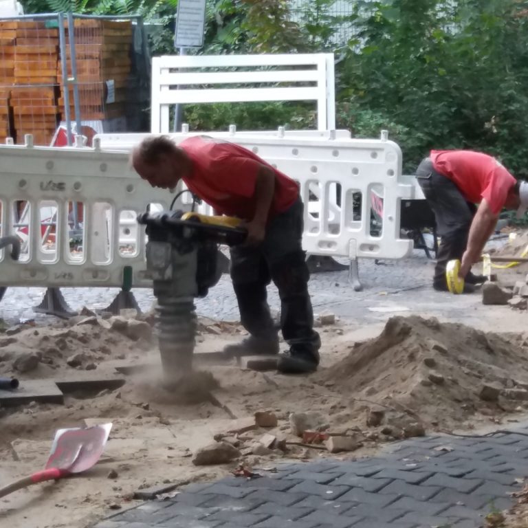Energetische Hausreinigung Arbeiter nutzen einen Rüttler, um Boden in einer Baustelle zu verdichten.