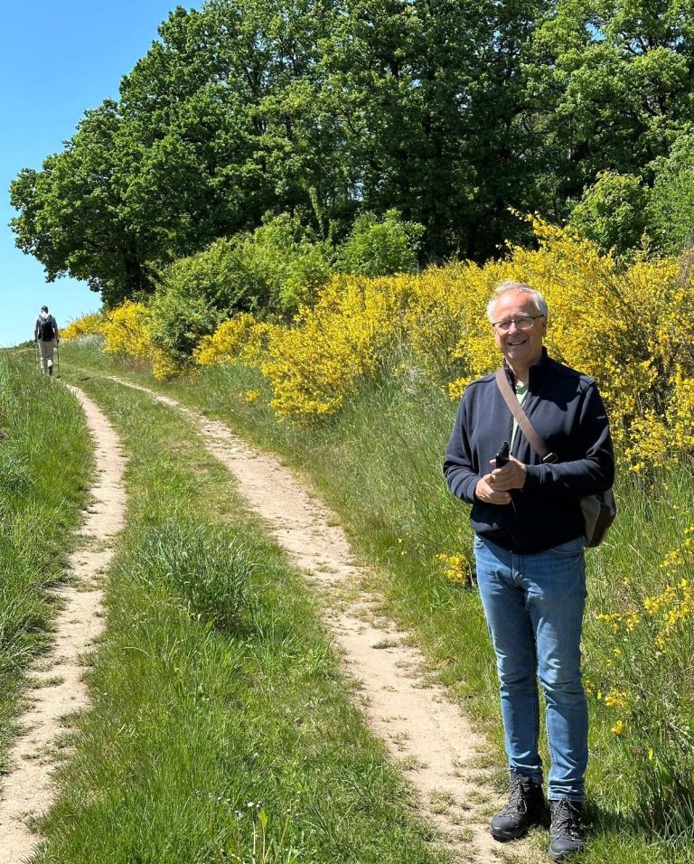 Werdegang von Andreas Bieler Mann mit Brille steht auf einem Weg, umgeben von gelben Blumen und Bäumen.
