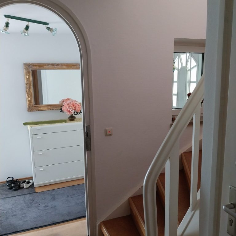 Eingangsbereich mit Treppe, Spiegel, Kommode und blühenden Pflanzen.